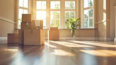 Stacked cardboard moving boxes in an empty, sunlit living room with bare hardwood floors